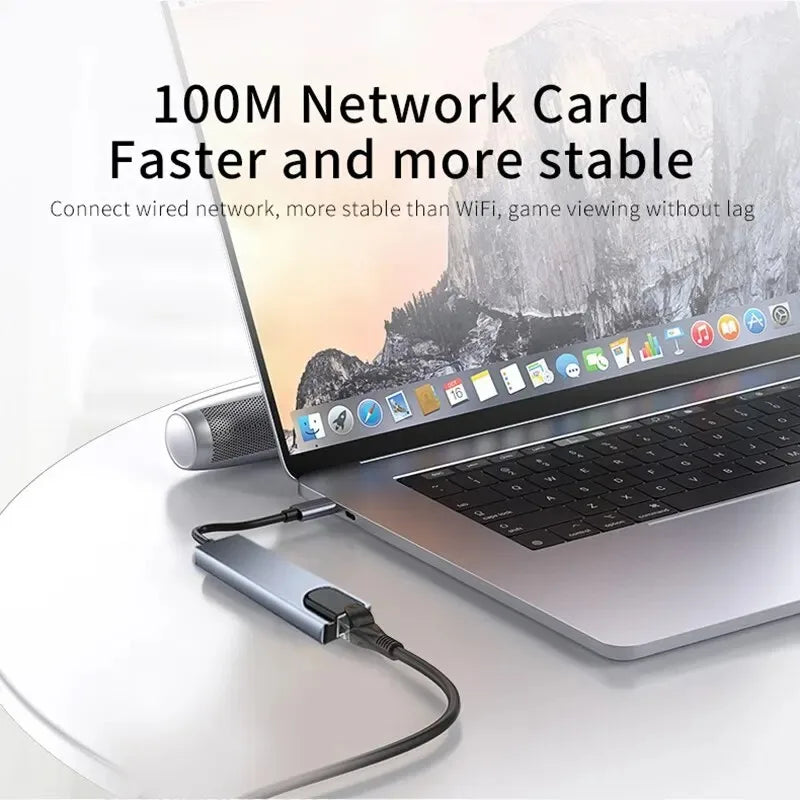A laptop is shown with a 100M network card adapter connected to a USB-C hub on a white surface.
