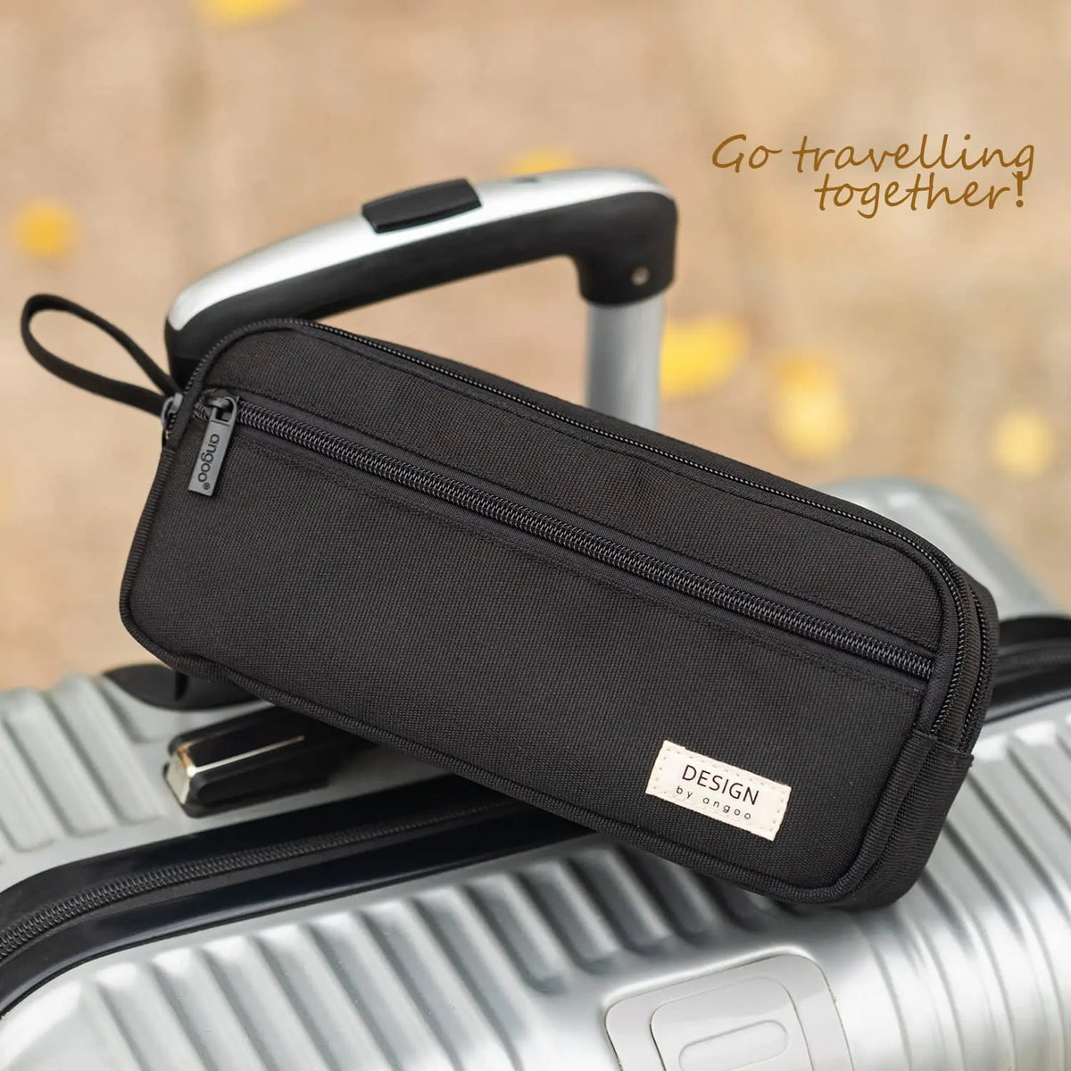A black multi-layer stationery storage pencil case is shown resting on a silver suitcase.