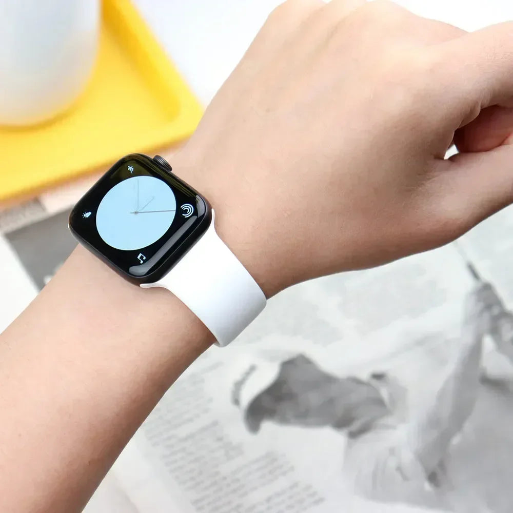 A hand wearing a white silicone sport band on an Apple Watch, with a yellow object in the background.