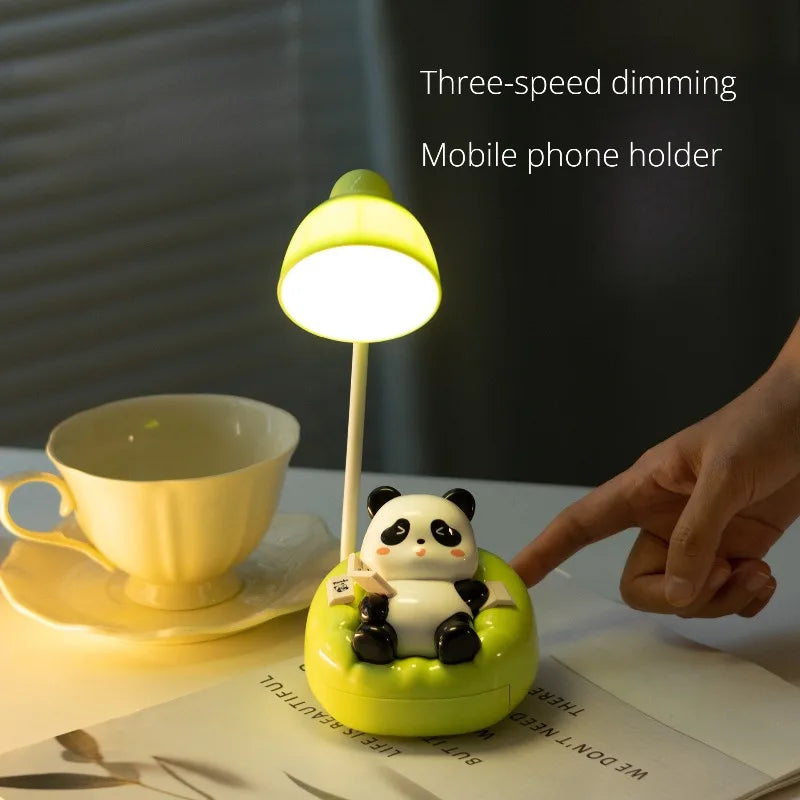 A yellow panda-shaped LED desk lamp with a mobile phone holder resting on a white notebook.