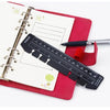 Rotes Notizbuch mit transparentem Lineal-Buchmarker und schwarzem Stift auf der Seite.