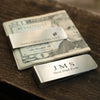 A silver engraved money clip resting on a stack of US dollar bills featuring a portrait and a thank you note.
