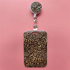 A leopard print retractable card holder clip for badges and IDs displayed against a pink background.