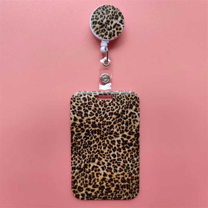 A leopard print retractable card holder clip for badges and IDs displayed against a pink background.