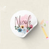 A white sticker featuring the name Nicole written in elegant script surrounded by pink and blue floral elements.