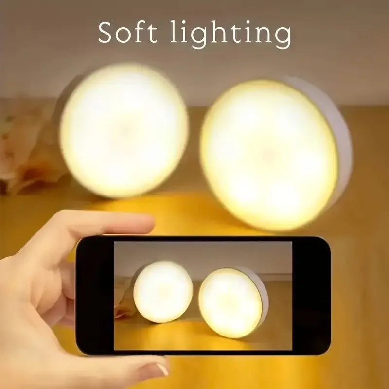 A hand holds a smartphone displaying a soft lighting motion sensor LED night light set illuminating a cabinet or wardrobe.
