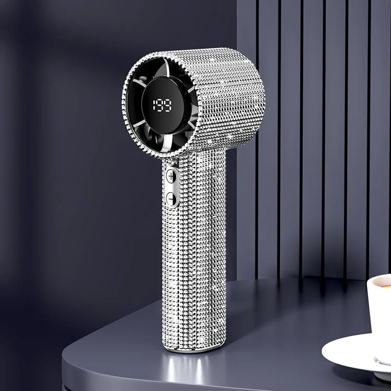 A silver sparkling diamond portable handheld fan with an LED display standing on a dark surface.