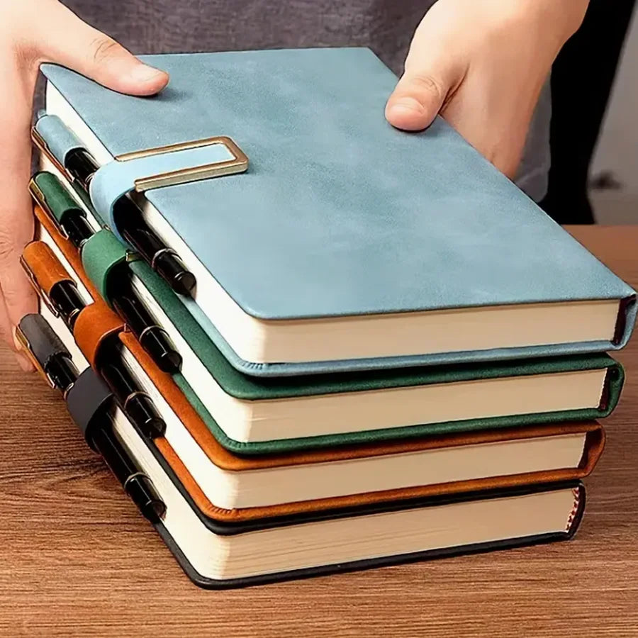 A stack of five A5 retro leather notebooks in shades of blue, green, and brown stacked on a wooden surface.