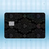 A black plastic card featuring a damask pattern and a square chip, set against a light blue striped background.