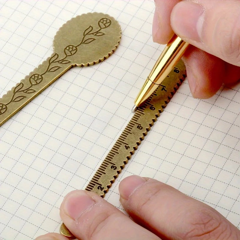 A hand is using a vintage brass straight ruler with a minimalist design to measure or mark something on a piece of graph pape