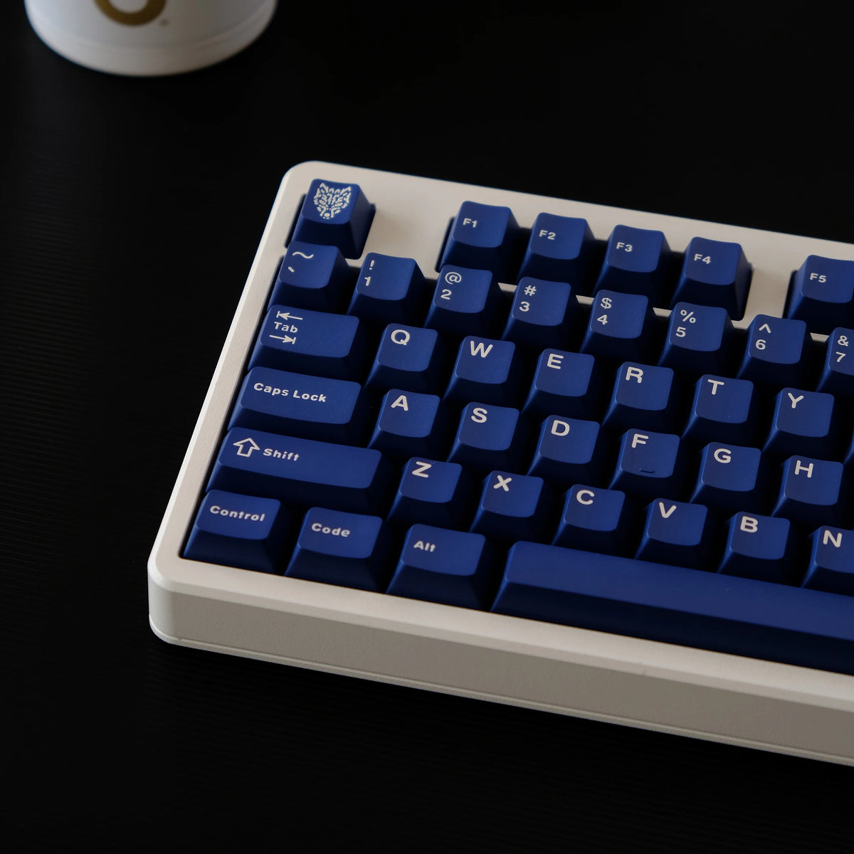 A close-up view of a white mechanical keyboard with dark blue PBT keycaps resting on a black surface.