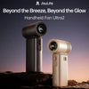 A handheld fan, the Jisulife Beyond the Breeze, Beyond the Glow model, is shown in a silver-gray color against a sunset backg
