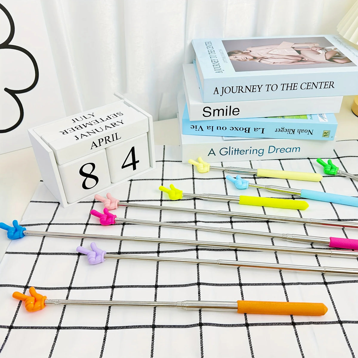 Un juego de cinco punteros retráctiles de profesor plateados con puntas de colores sobre un paño a cuadros blanco y negro.