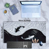 A gaming mouse pad featuring a black and white koi pattern with fish silhouettes, placed next to a laptop and a computer mous