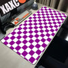 A purple and white checkered desk mat is displayed on a wooden table next to a keyboard and gaming controller.