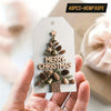 A hand holds a farmhouse Christmas gift tag featuring wood grain and pinecone cutouts with hemp rope.