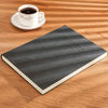 A dark gray notebook lies on a wooden surface next to a white cup and saucer.
