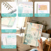 A spiral bound planner with monthly tabs and inner pocket for stickers shown open on a wooden surface.