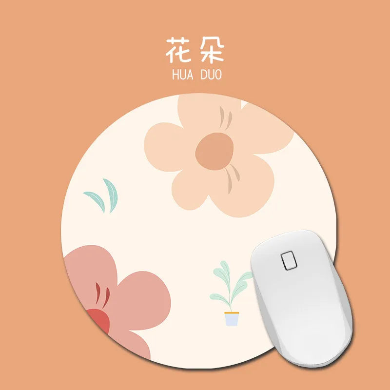 A round, light pink mouse pad with a floral design featuring a peach-colored flower and green leaves.