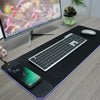 A black mousepad with a built-in light, featuring a keyboard and a smartphone charging area.