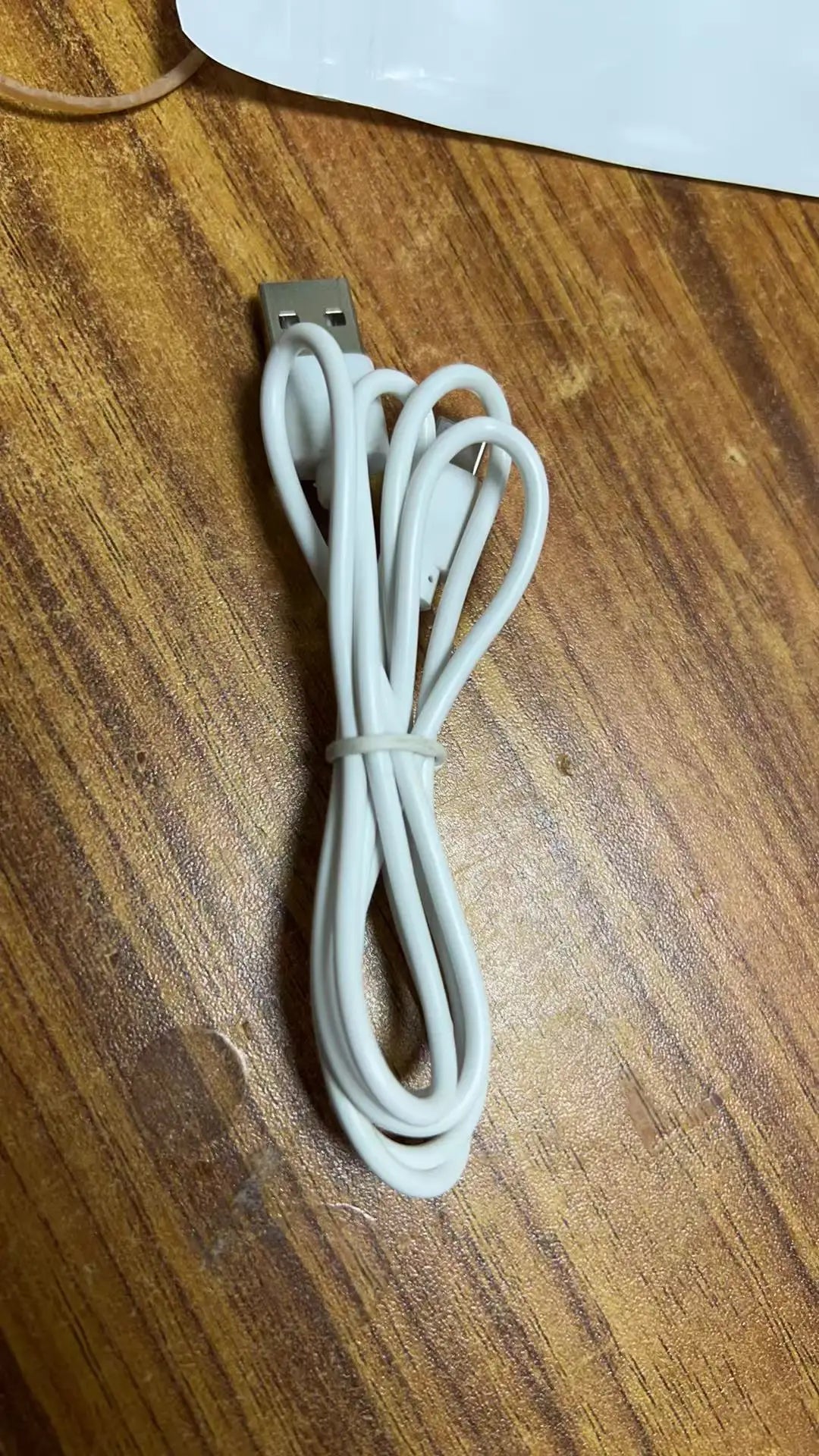 A white charging cable for True Buds 5 Bluetooth 5.3 wireless earphones lying on a wooden surface.