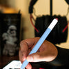 Une main tient un stylo bleu clair écrivant sur un écran de tablette avec un casque noir visible en arrière-plan.