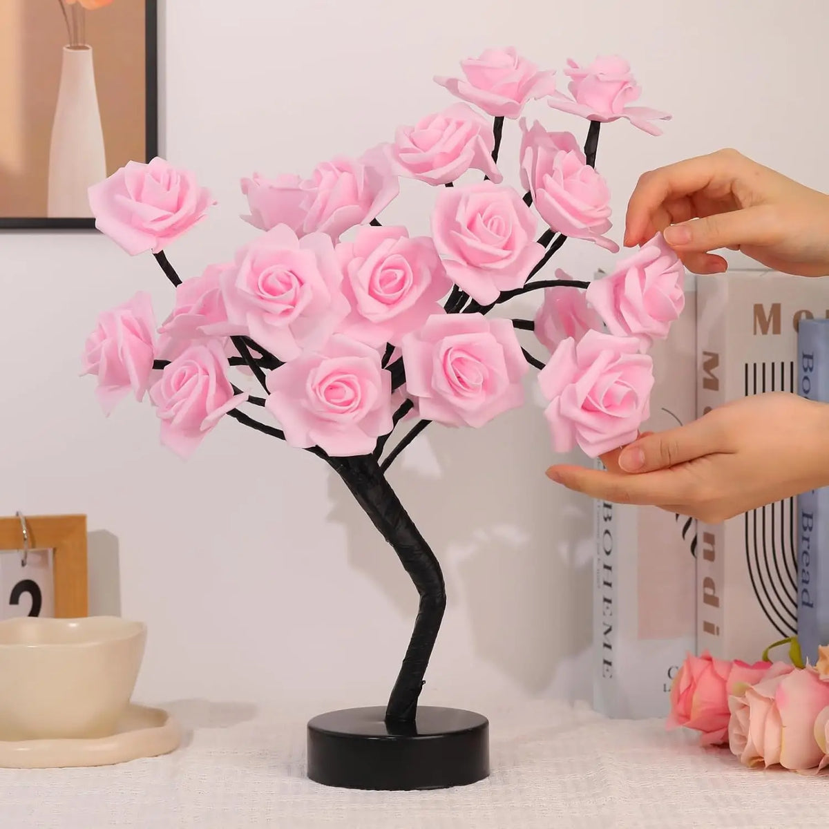 Pink artificial rose tree with black branches and pink roses being held by hands
