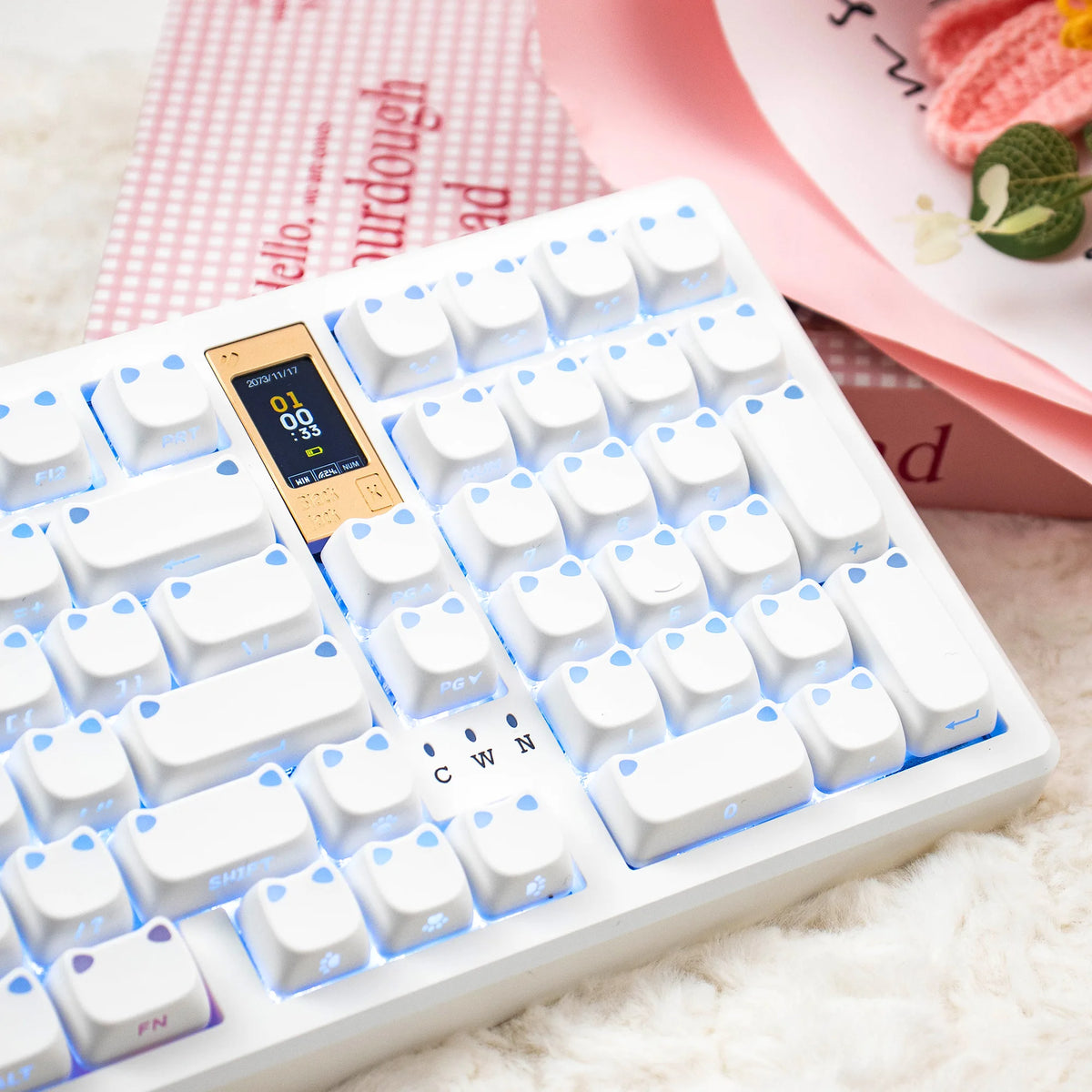 Weiße mechanische Tastatur mit hellblauen Beleucht-Tasten und rosa Hintergrund mit Katzen-Themen-Artikeln.