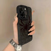 A hand holds a black phone case featuring a spider web design and a silver wristwatch against a light background.
