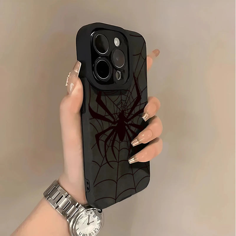 A hand holds a black phone case featuring a spider web design and a silver wristwatch against a light background.