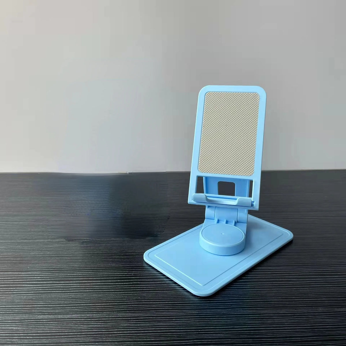 A light blue desktop stand for a phone or tablet with a mesh screen, resting on a dark surface.