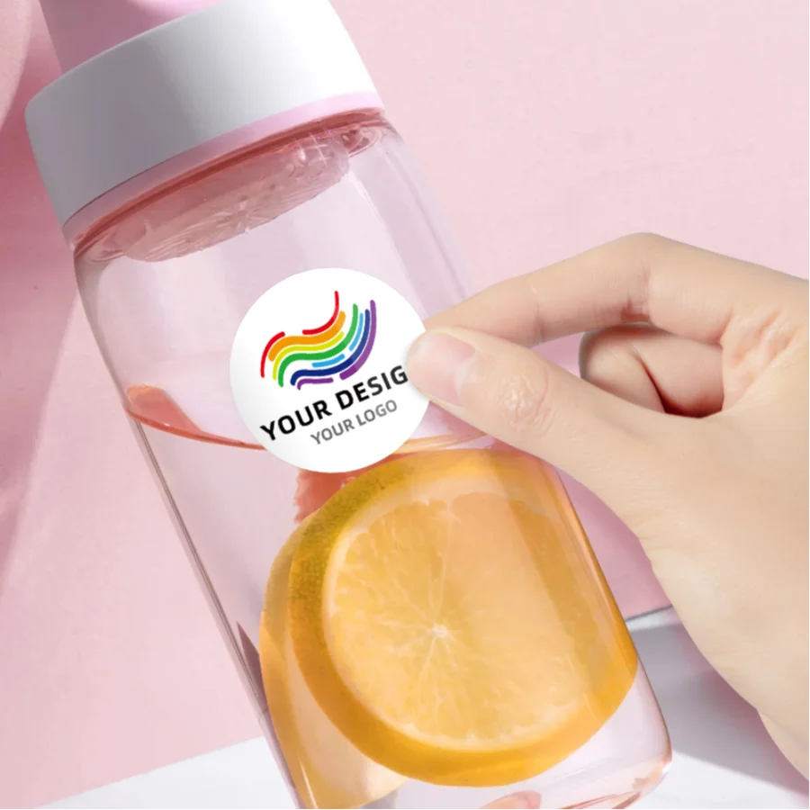 A hand holds a pink bottle of liquid with a colorful rainbow sticker design on the label.