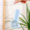 A hand is holding a light blue portable rechargeable mini handheld fan with a mesh grille.