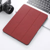 A red retro marbling skin for an iPad Pro placed next to a silver camera and a white laptop keyboard.