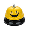 A yellow classic metal service bell with a smiling face and a silver top, sitting on a black base.