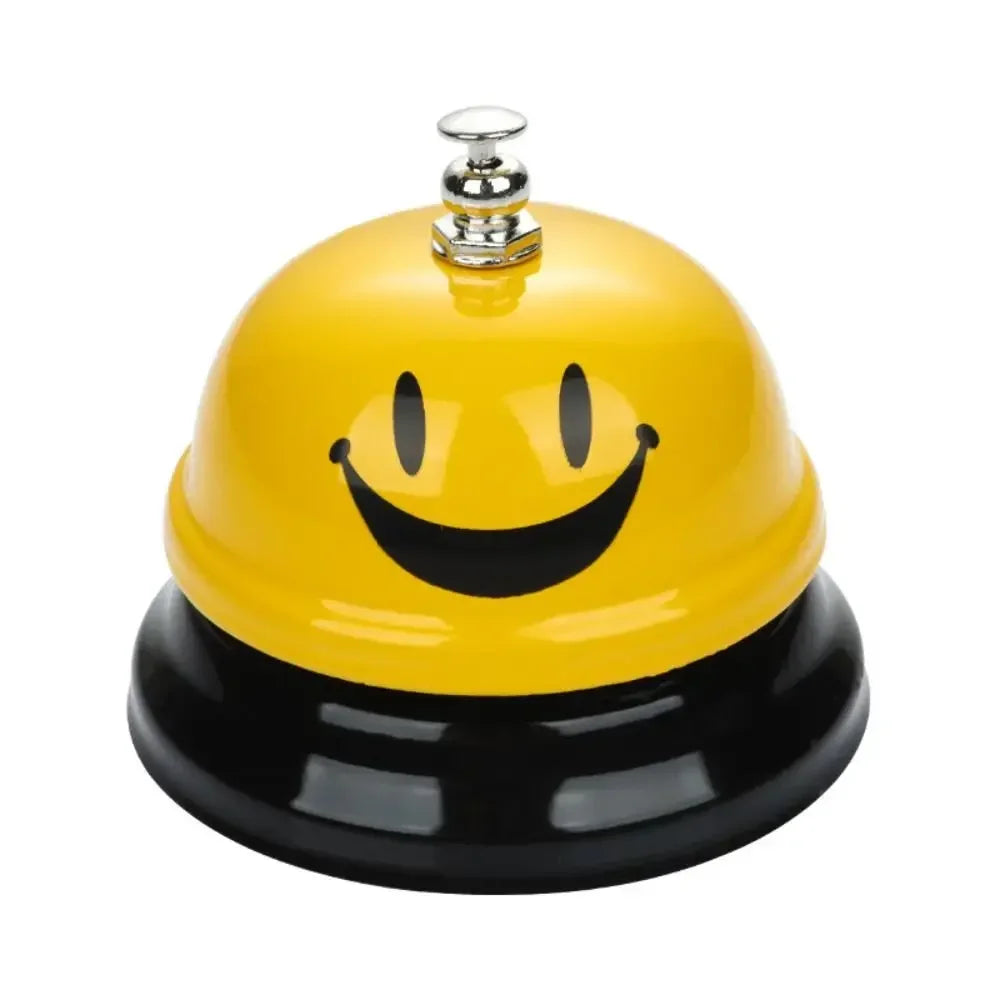 A yellow classic metal service bell with a smiling face and a silver top, sitting on a black base.