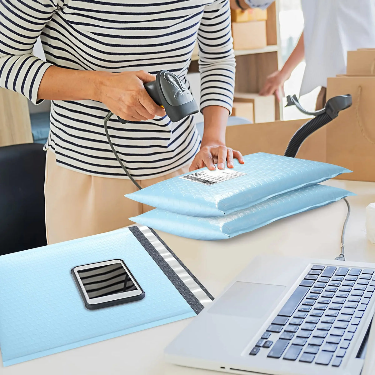 Eine Person bereitet opake blaue Luftpolsterumschläge für den Versand auf einem Schreibtisch neben einem Laptop vor.