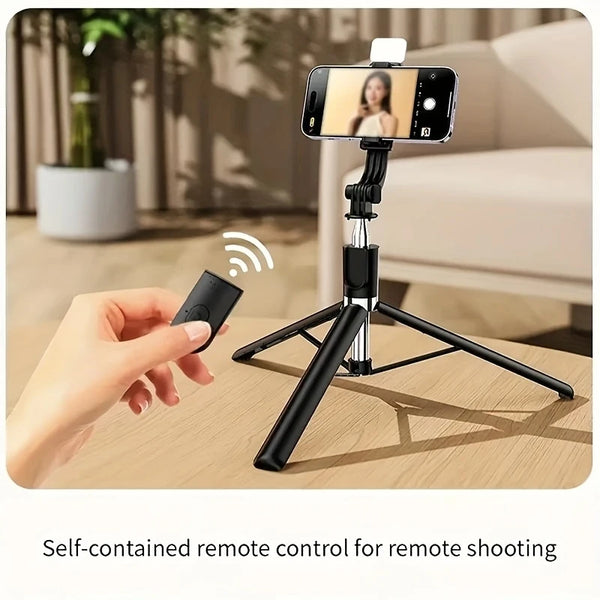 A hand holds a black wireless remote control for a professional extendable selfie stick tripod setup.