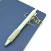 A light green magnetic pen clip with a yellow wire loop rests on a dark blue notebook page.