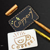 A set of metallic brush marker pens and a tag with the word Copper on a black background.