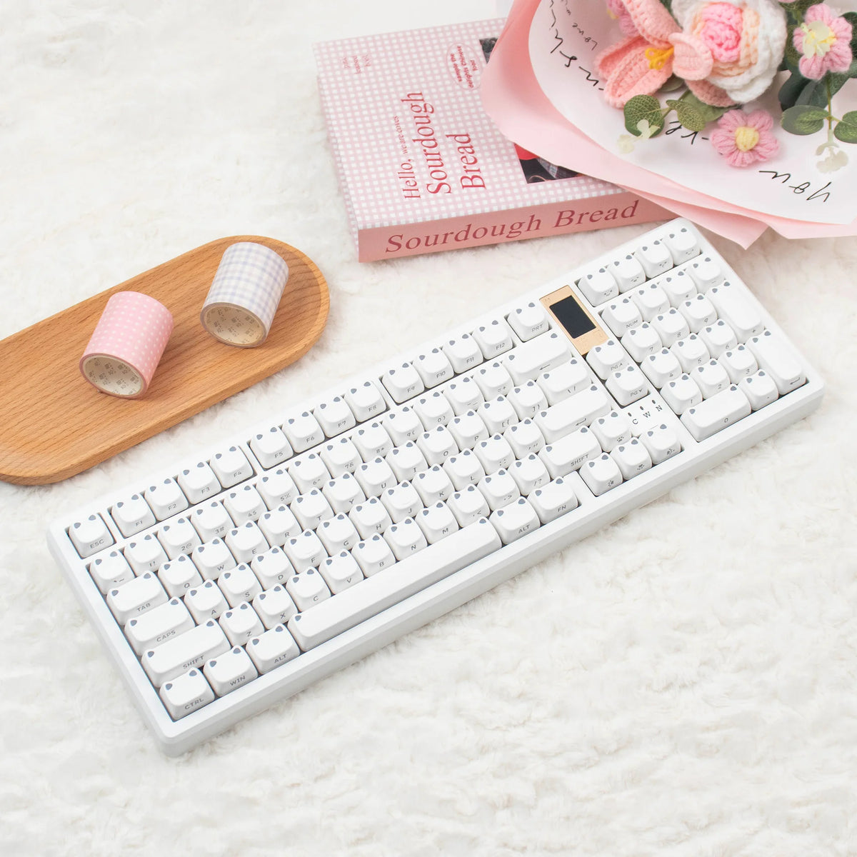 Weiße mechanische Tastatur mit rosa Tastenkappen neben einem Holztray und rosa Verpackung