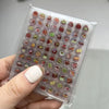 A hand holds a clear plastic storage book filled with 2400 mini stickers featuring various cute patterns and colors.