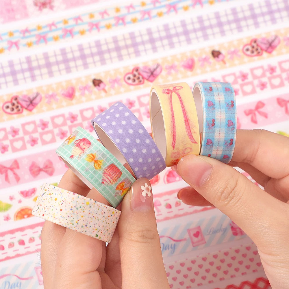 A hand holds a set of three rolls of pastel colored washi tape featuring butterfly and gingham patterns on a pink background.