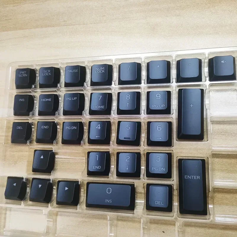 A close-up view of a clear plastic case containing replacement keycaps for a Dell Alienware AW510K keyboard.