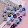 A collection of handmade acrylic flower beads in various shades of blue and purple arranged on a white card.