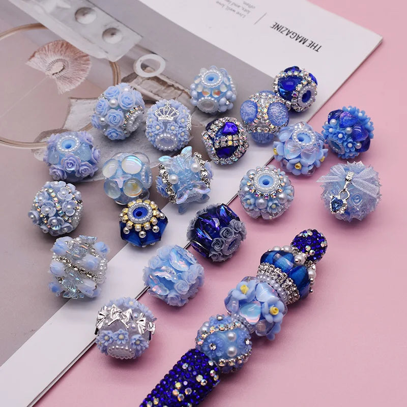 A collection of handmade acrylic flower beads in various shades of blue and purple arranged on a white card.