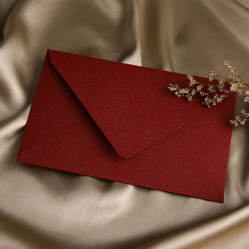 Ein tiefroter Umschlag liegt auf glattem beige Satin mit einem zarten goldenen Zweig.