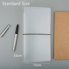 A clear PVC cover for a standard travelers notebook shown next to a pen and a brown notebook.