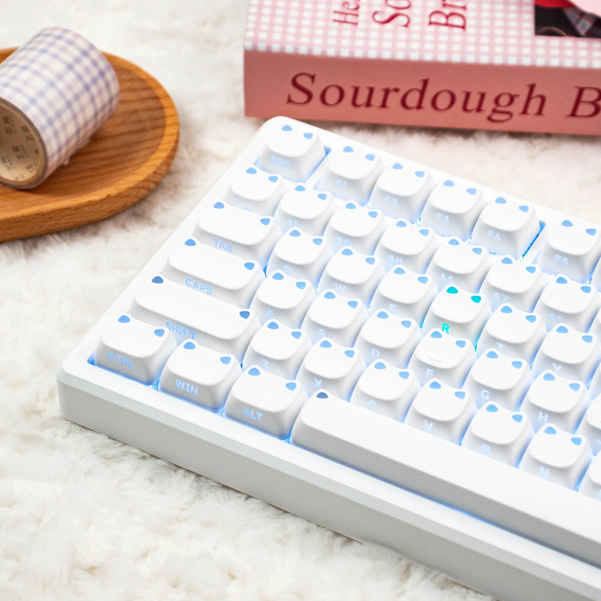 Eine weiße mechanische Tastatur mit hellblauen Tastenkappen neben einem Holzgegenstand und einem Buch.
