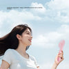 A woman is holding a pink portable foldable rabbit mini fan against a bright sky.